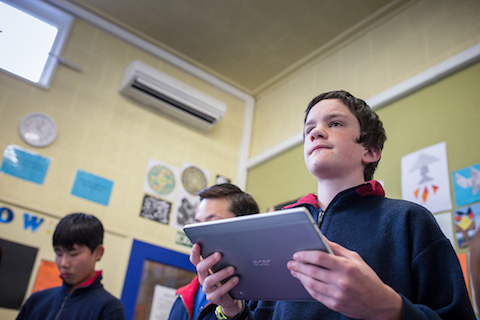 A boy in a classroom holding a laptop..