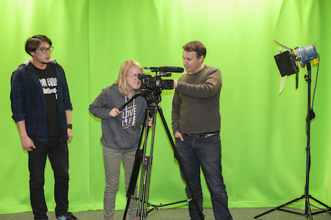 Two young people being shown how to use a camera in a studio by an older man..