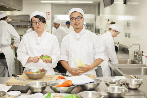 A young man and woman in chef training preparing food. .