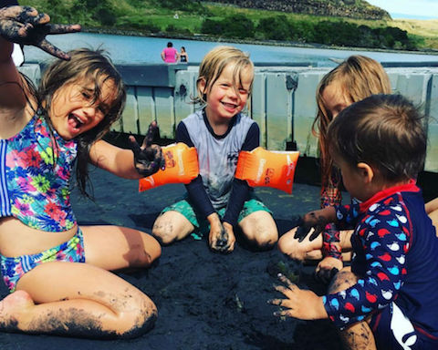 A group of children playing in black sand at the beach..